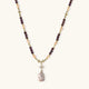 Gold necklace with iridescent baroque pearl pendant, purple amethyst beads, and crystal star charm on cream background