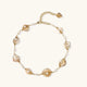 Gold-plated necklace with wire-wrapped shell pieces and freshwater pearls on neutral background, adjustable chain visible.